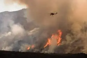 Helicopter battling a fierce wildfire amidst smoke and flames.