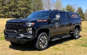 A black Chevrolet pickup truck marked "District Chief" and "Fire Department," parked on grass with trees in the background. It has emergency lights and a protective grille.