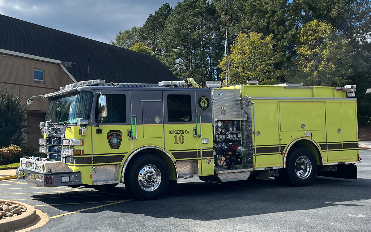 A yellow fire truck marked "Engine Co 10" parked outside near a brick building and trees. The truck has various firefighting equipment visible on its side.