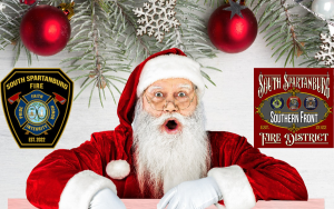 Santa Claus with a surprised expression is under a decorated pine branch with red baubles. To the left is a South Spartanburg Fire Department badge, and to the right is a sign for the South Spartanburg Southern Front Fire District.